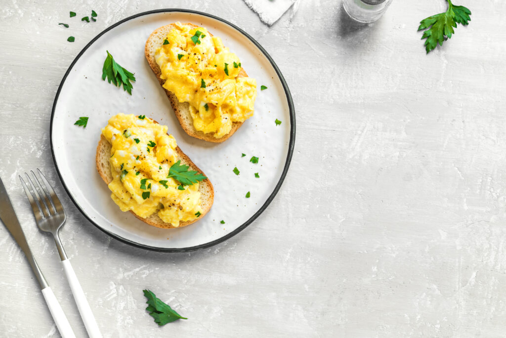 Scrambled Eggs on toasted bread for healthy breakfast or brunch, top view, copy space. Homemade  meal recipe - scrambled eggs toasts on blue background.